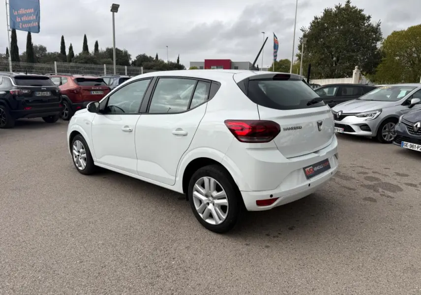 Vue 3/4 arrière droite d'une Dacia Sandero blanche 2021 avec vitres surteintées et feux arrière allumés.
