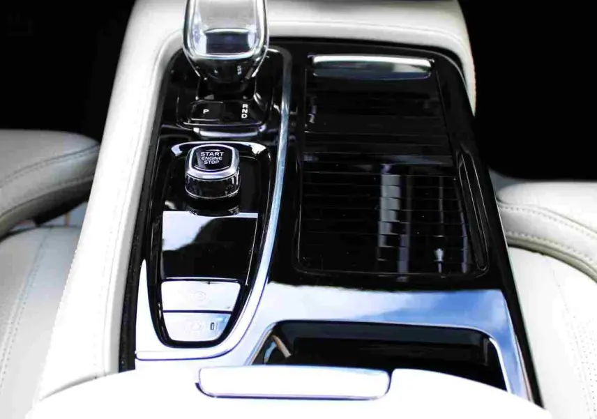 Vue rapprochée de la console centrale noire brillante avec levier de vitesse cristal et sièges cuir clair d'une Volvo S60 2024.