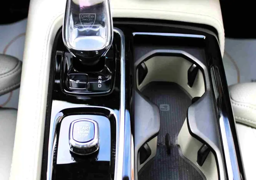 Gros plan sur la console centrale beige du Volvo S60 2024 avec levier de vitesses cristal et bouton start/stop.