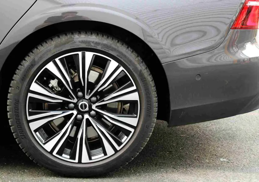 Gros plan sur la roue arrière droite et le pare-chocs gris métal d'une Volvo S60 T6 hybride rechargeable 2024.