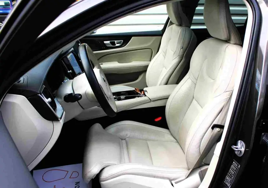 Intérieur clair de la Volvo S60 T6 AWD 2024, vue côté conducteur avec sièges cuir beige et tableau de bord moderne.