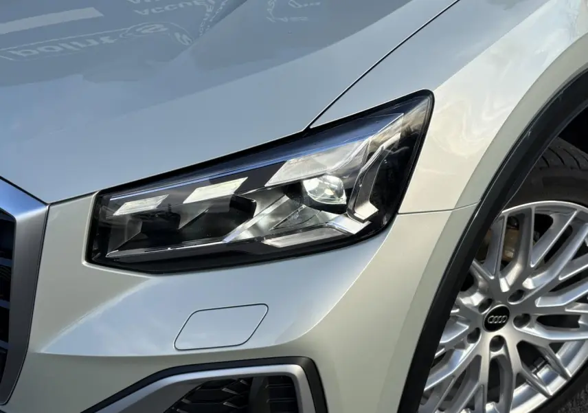 Gros plan sur le phare avant droit et la roue argentée d’un Audi Q2 35 TDI S-Line couleur argent rosé.
