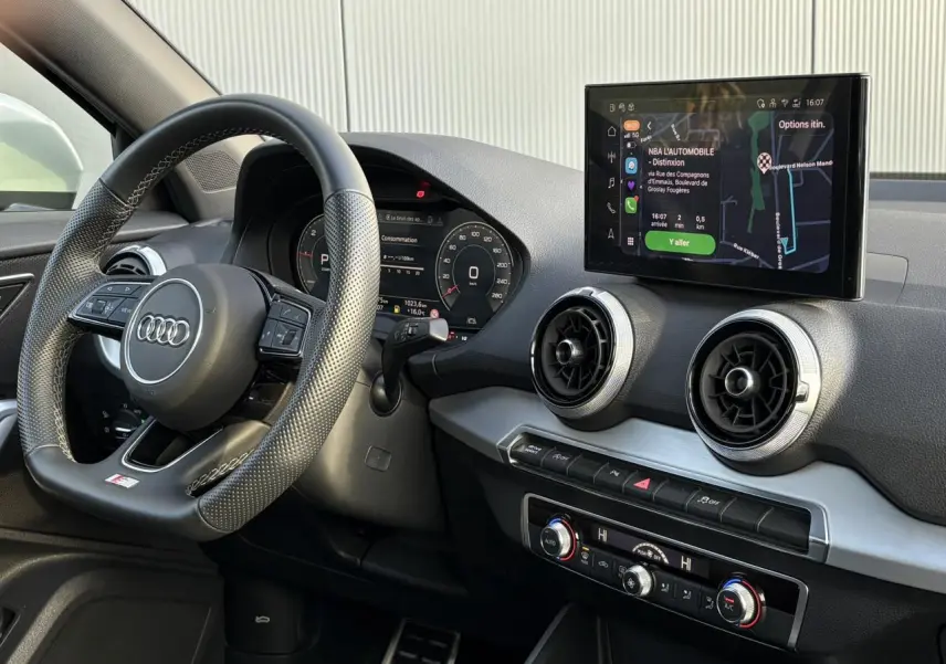 Vue intérieure côté conducteur de l'Audi Q2 35 TDI S-Line 2025, volant cuir et écran tactile MMI avec navigation.