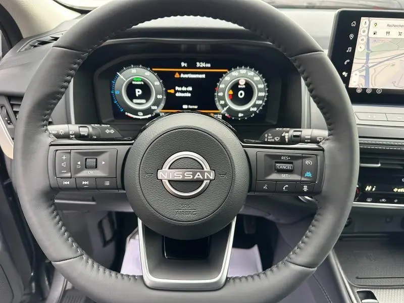 Vue rapprochée du volant noir du Nissan Qashqai Hybrid e-POWER 2025 avec tableau de bord numérique et écran tactile visible.
