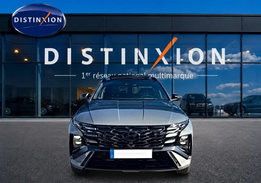 Vue avant d'un Hyundai Tucson 2026 gris shadow avec calandre noire et phares LED, devant une vitrine Distinxion.