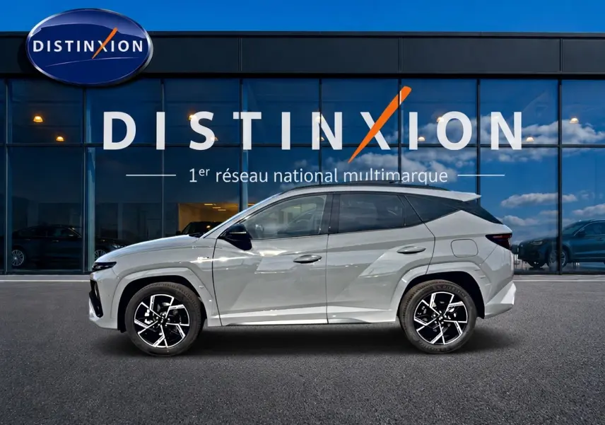 Vue de profil côté gauche du Hyundai Tucson 2026 gris shadow avec jantes alliage distinctives devant une vitrine Distinxion.