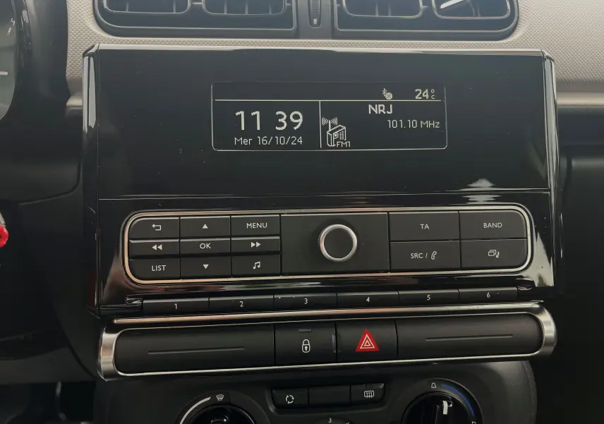 Détail de la console centrale noire de la Citroën C3 blanche 2017, affichant l'horloge et la radio NRJ FM.