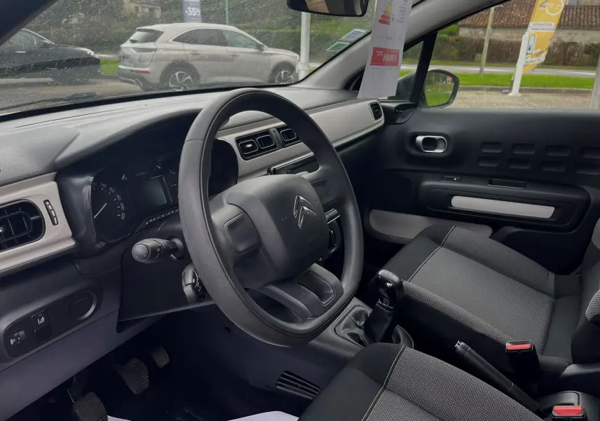 Intérieur de la Citroën C3 blanc 2017, vue côté conducteur montrant le volant, tableau de bord et sièges tissu gris-noir.