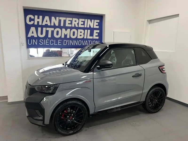 Vue 3/4 avant droit d'une LIGIER JS50 SPORT ULTIMATE E5+ gris avec toit noir et jantes noires en intérieur showroom.