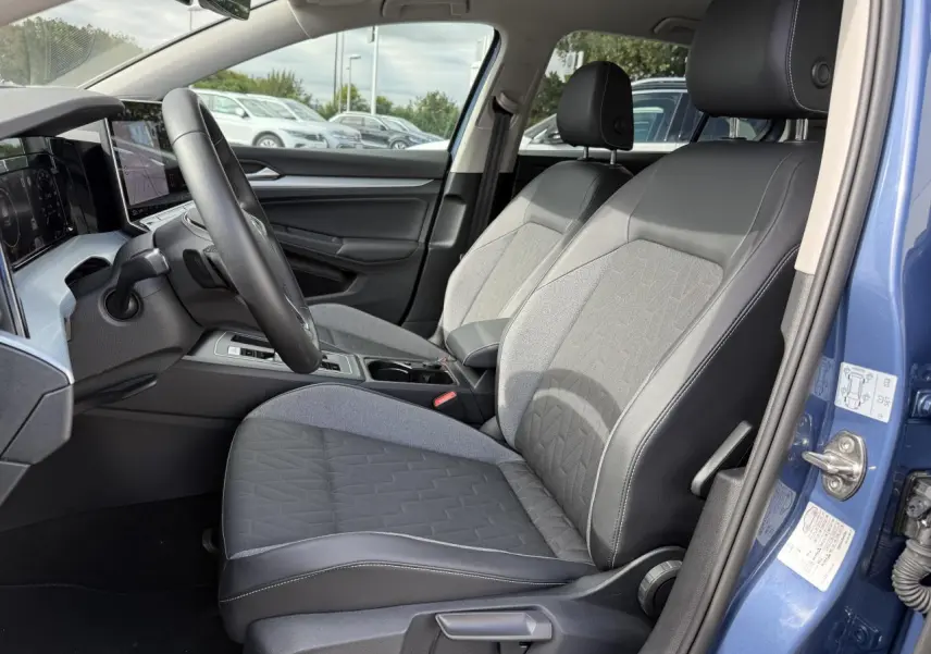 Vue intérieure côté conducteur de la Volkswagen Golf 2024 bleu anémone, sièges tissu et cuir noir avec tableau de bord digital.