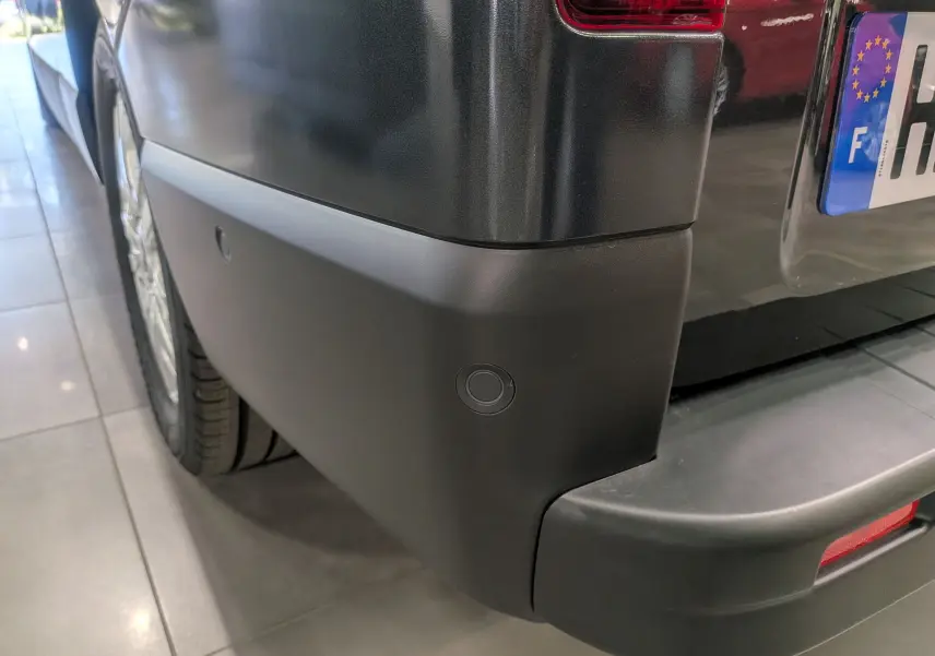 Gros plan sur le pare-chocs arrière gris comète du Renault Trafic Combi avec capteur de recul visible.