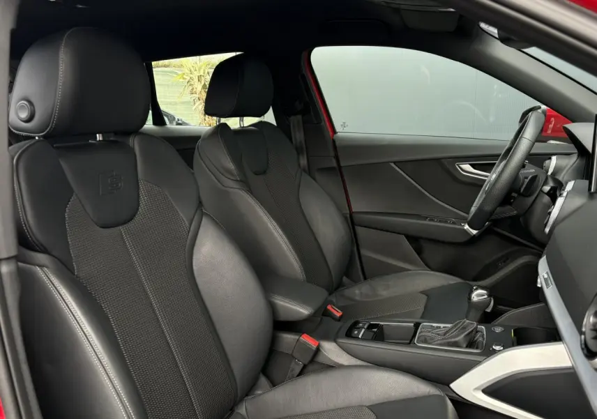 Vue intérieure côté conducteur de l'Audi Q2 rouge 2025, sièges sport cuir/tissu noirs avec logo S embossé.