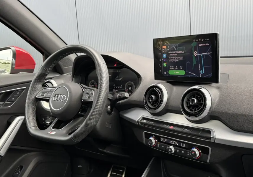 Vue intérieure côté conducteur de l’Audi Q2 rouge 2025, avec volant cuir multifonction et écran MMI navigation visible.