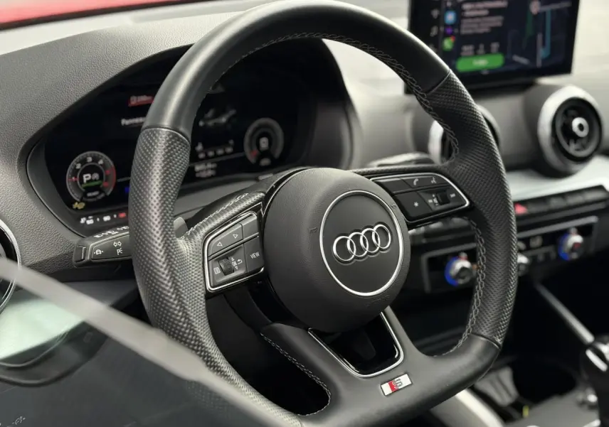 Vue rapprochée du volant cuir noir multifonction avec logo Audi et badge S-Line dans l’habitacle du Q2.