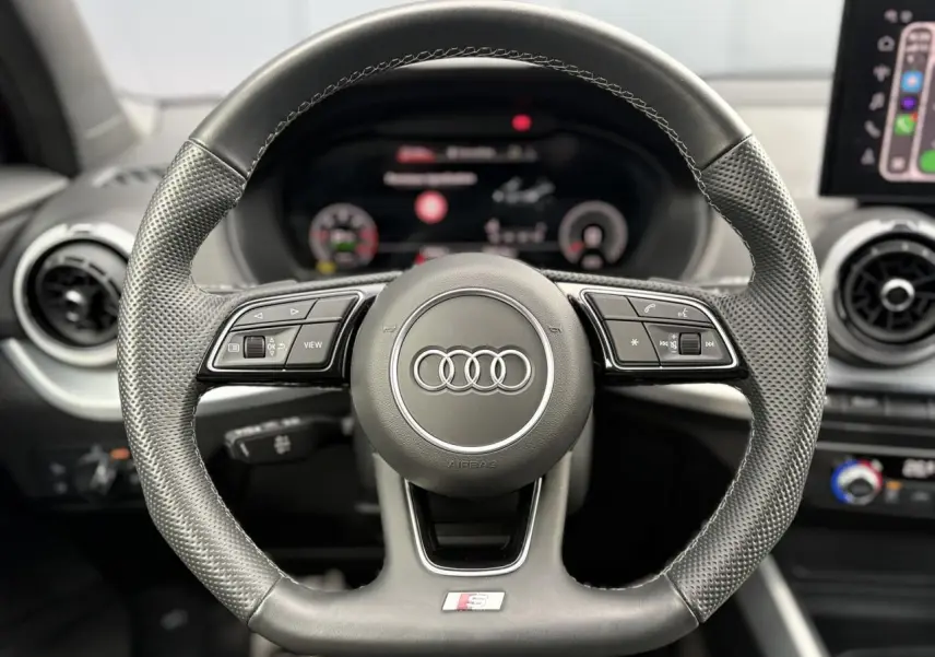 Volant multifonction en cuir noir avec logo Audi et badge S-Line, vue frontale centrée sur le volant.