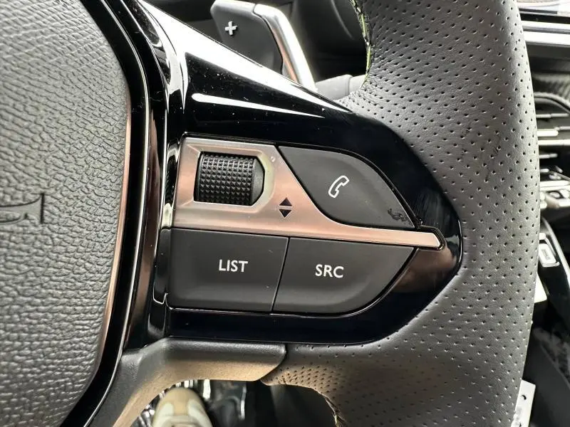 Gros plan sur les commandes gauche du volant perforé gris du Peugeot 2008 1.2 Hybrid 145ch GT 2025, avec molette et boutons fonctionnels.