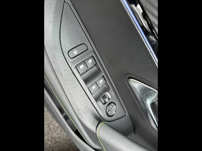 Gros plan sur la porte côté gauche du Peugeot 2008 gris 2025, montrant les commandes des vitres et rétroviseurs avec surpiqûres vertes.