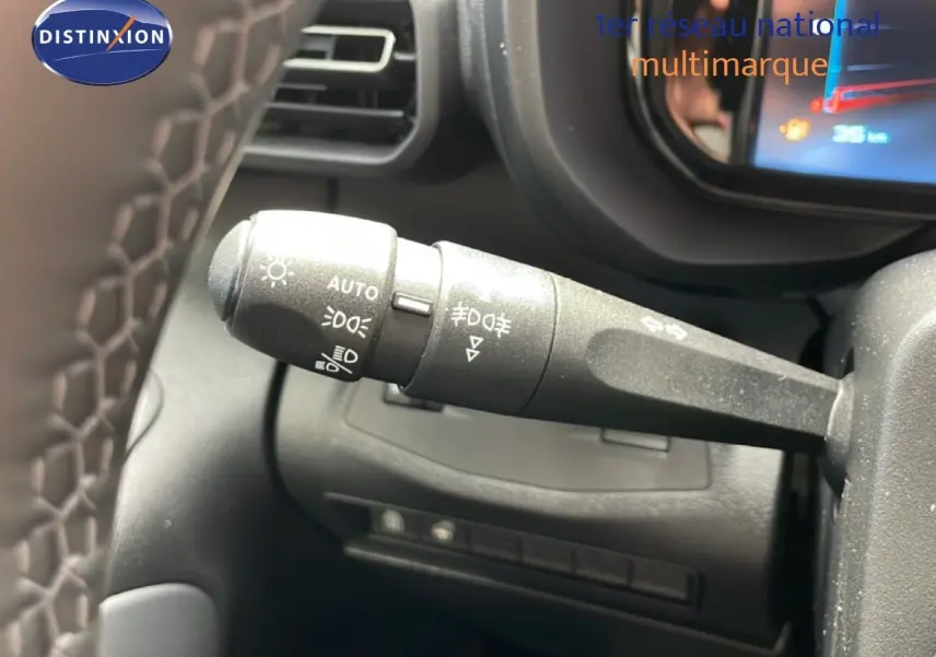 Gros plan sur la commande des feux au volant du Citroën Berlingo gris, avec tableau de bord numérique en arrière-plan.