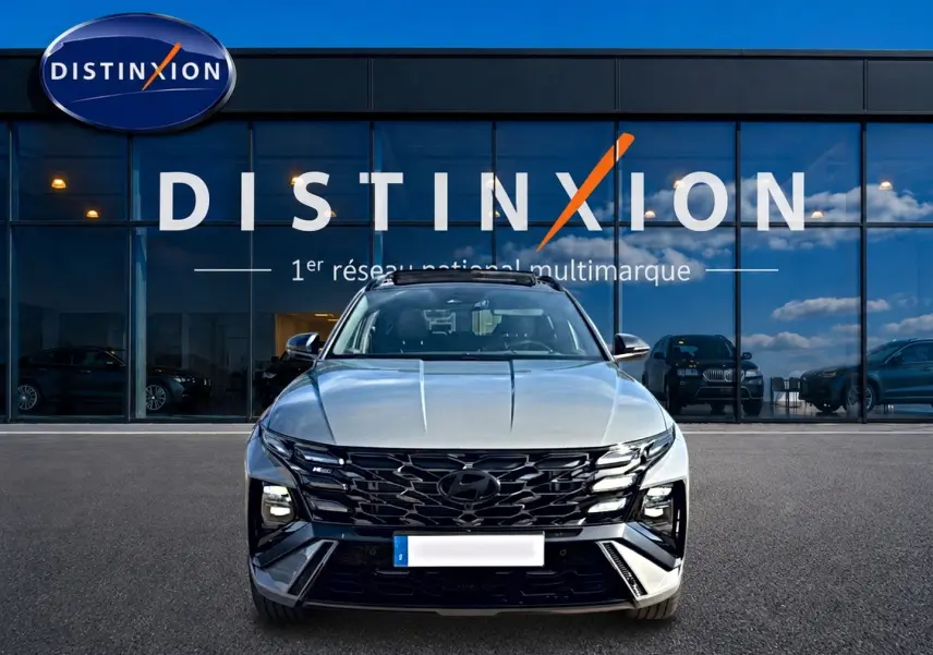 Vue avant d'un Hyundai Tucson gris shadow 2026 avec calandre noire et toit panoramique devant un showroom Distinxion.