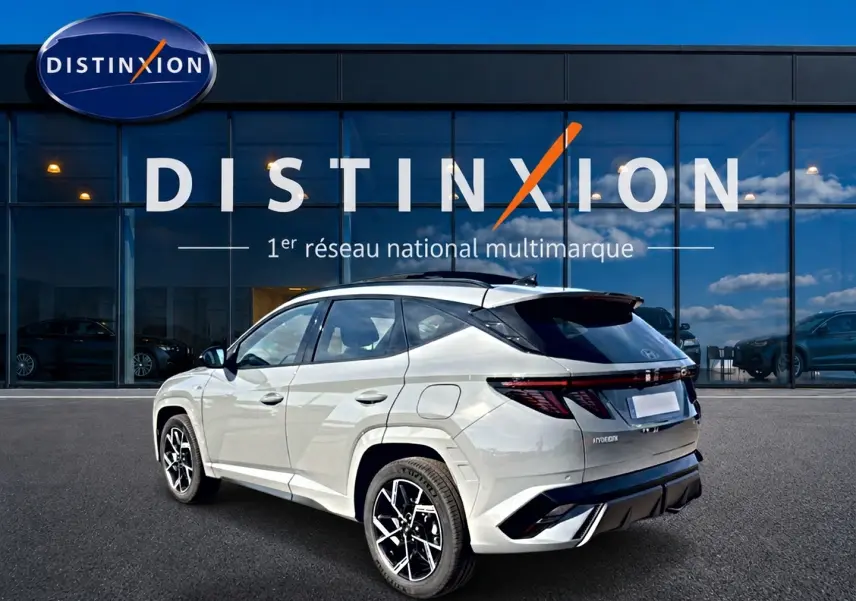 Vue 3/4 arrière du Hyundai Tucson gris shadow avec jantes alu noires et toit panoramique, devant une vitrine Distinxion.