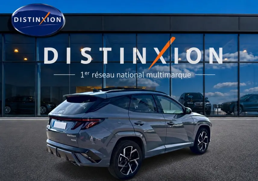 Vue 3/4 arrière droite du Hyundai Tucson gris shadow avec jantes alu noires et toit panoramique devant un showroom Distinxion.