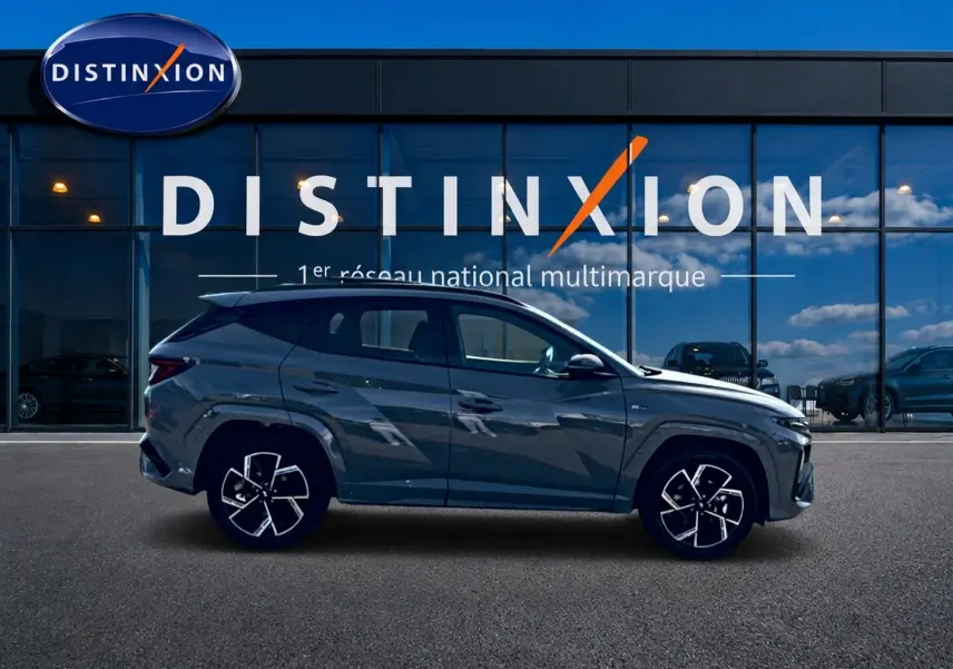Hyundai Tucson 2026 gris shadow en profil droit devant une vitrine Distinxion, jantes alu noires et chromées visibles.