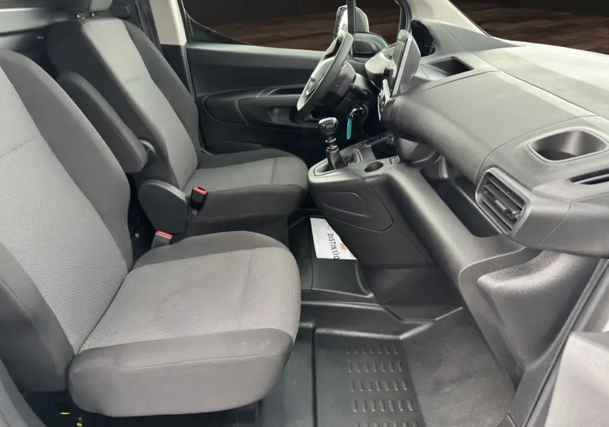 Intérieur du Peugeot Partner 2022 vu côté conducteur, sièges tissu gris et tableau de bord noir avec boîte manuelle.