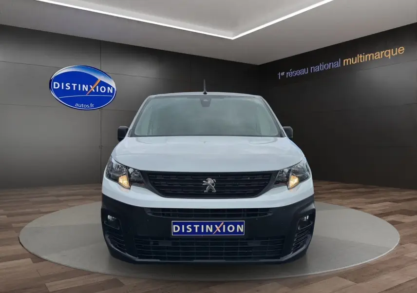 Vue frontale d'un Peugeot Partner blanc 2022 avec calandre noire et phares allumés en showroom.