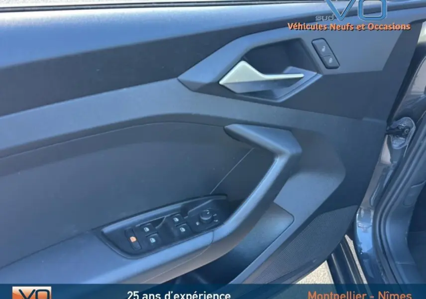 Vue rapprochée de la porte avant gauche gris foncé d'une Audi A1 Sportback 2020 avec commandes électriques et poignée argentée.