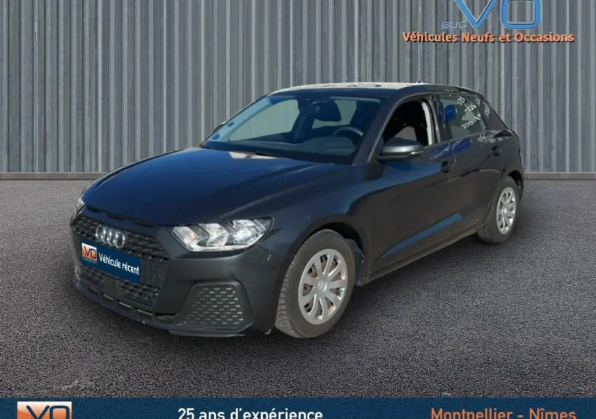 Audi A1 Sportback gris foncé vue 3/4 avant droit sur fond neutre avec logo VO en arrière-plan.