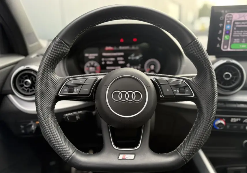 Gros plan sur le volant sport en cuir noir de l'Audi Q2 35 TDI S-Line avec commandes multifonctions et logo S.