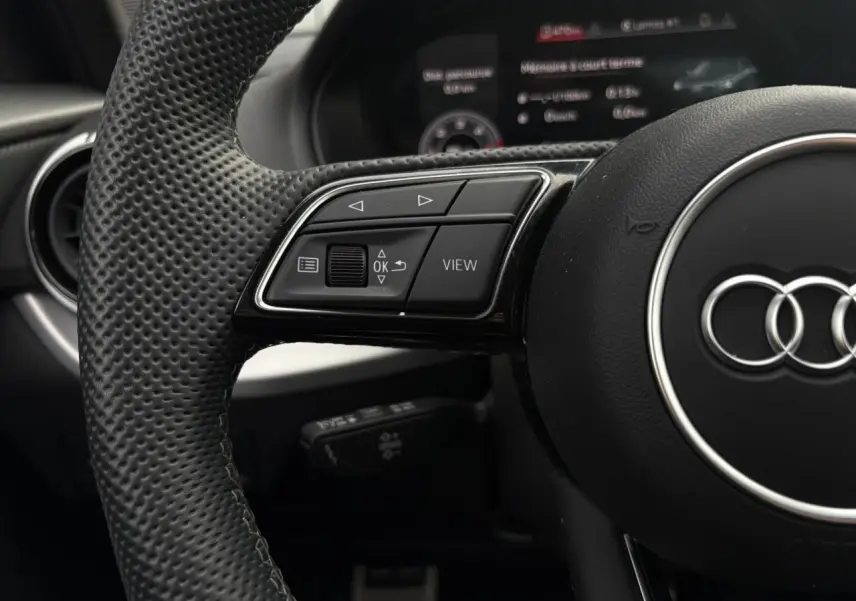 Gros plan sur le volant cuir perforé de l'Audi Q2 35 TDI S-Line avec commandes multifonctions et logo Audi central.