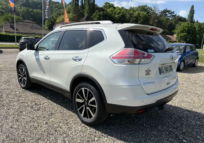 Nissan X-Trail blanc 2016 en 3/4 arrière droit, avec jantes alliage et vitres teintées, stationné sur un parking extérieur.