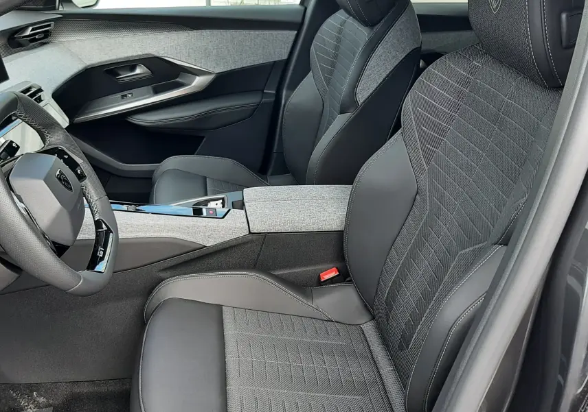 Vue intérieure côté conducteur du Peugeot 3008 gris titane 2026, sièges en tissu et cuir avec logo Peugeot brodé.