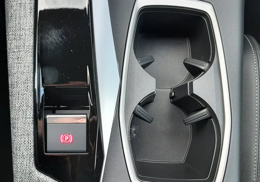 Gros plan sur la console centrale noire et grise du Peugeot 3008 hybride, avec porte-gobelets et bouton frein à main électronique.
