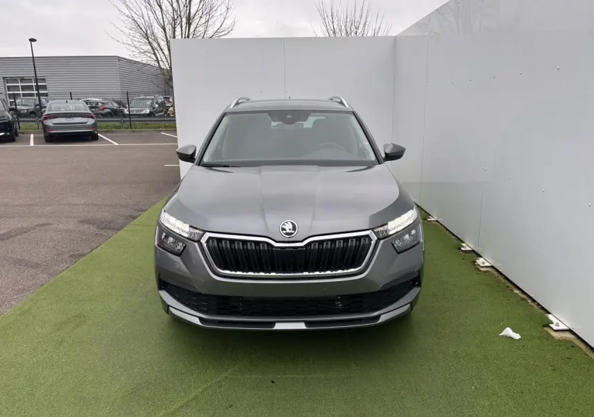 Vue avant d'un Skoda Kamiq gris graphite métal avec calandre noire et feux LED allumés sur fond urbain.