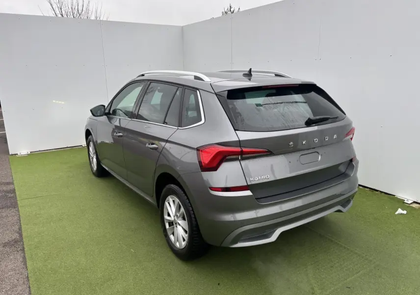 Vue 3/4 arrière droite d'un Skoda Kamiq gris graphite métallisé avec feux arrière LED et barres de toit argentées.