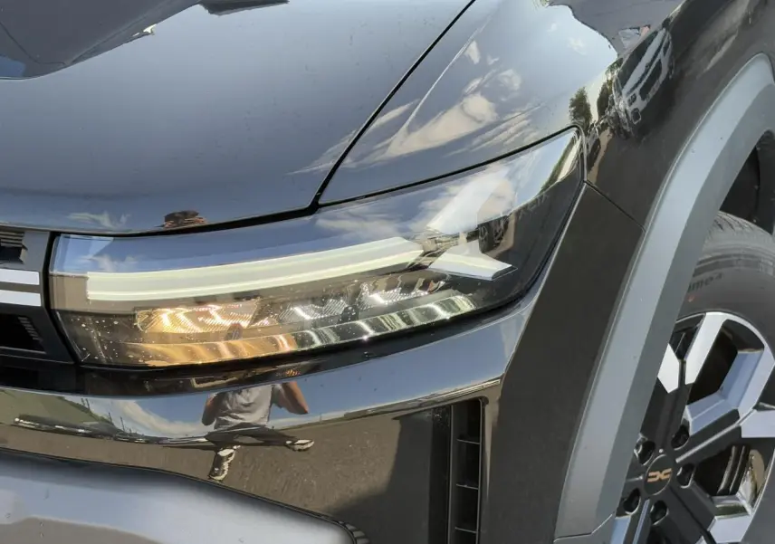 Gros plan sur le phare avant droit et la roue alliage 17" du Dacia Duster noir nacré 2025.