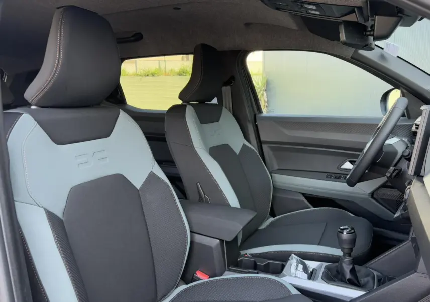 Vue intérieure côté conducteur du Dacia Duster 2025, sièges bicolores avec surpiqûres et levier de vitesses manuel.