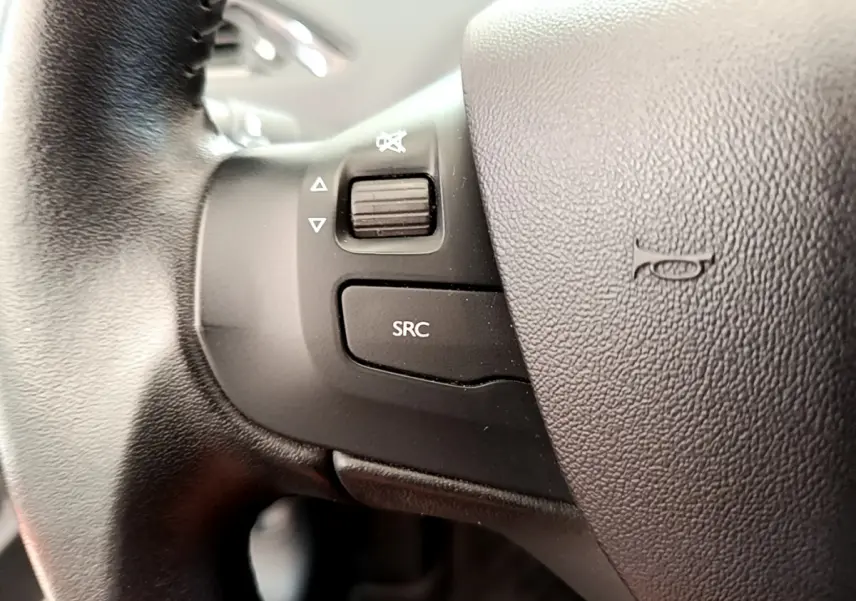Gros plan sur les commandes gauche du volant cuir de la Peugeot 208 Puretech 82 Signature 2019, avec bouton SRC et molette sonore.