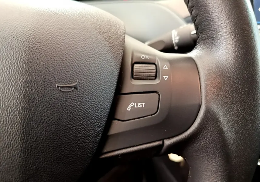 Gros plan sur les commandes du volant cuir de la Peugeot 208 Puretech 82 Signature, version essence blanche de 2019.