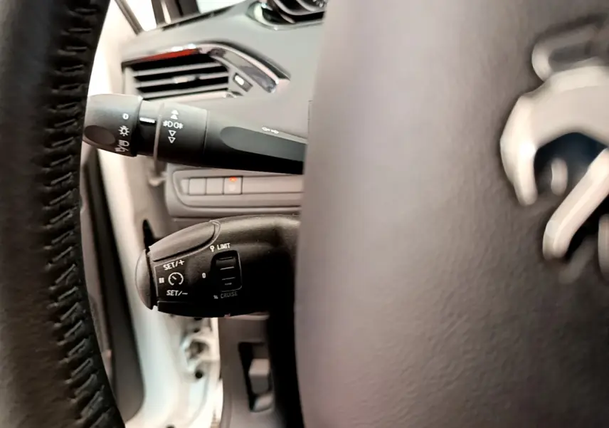 Détail du volant cuir et commandes de régulateur de vitesse sur Peugeot 208 blanc, vue côté gauche intérieur.
