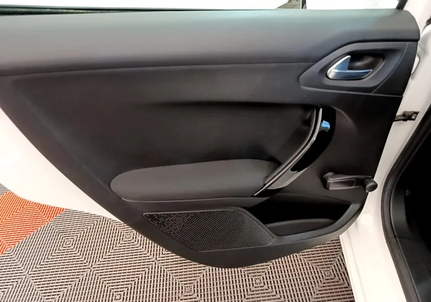 Vue rapprochée de la porte avant gauche noire d’une Peugeot 208 blanche, mettant en valeur la poignée intérieure chromée.
