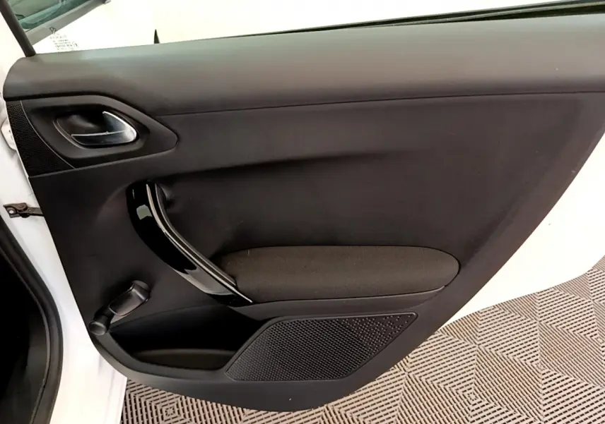 Vue intérieure de la porte côté gauche d'une Peugeot 208 blanche, avec poignée noire brillante et tissu noir.