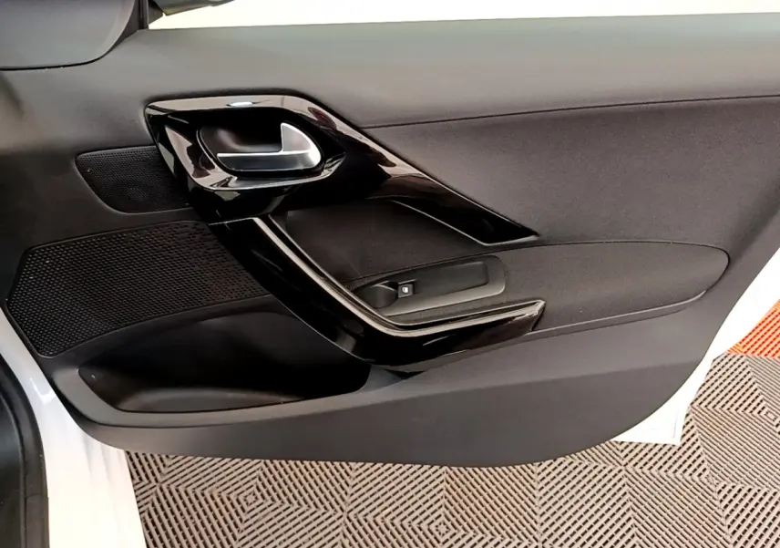 Gros plan sur la porte côté gauche blanche d'une Peugeot 208 Puretech 82 Signature avec poignée intérieure noire brillante.