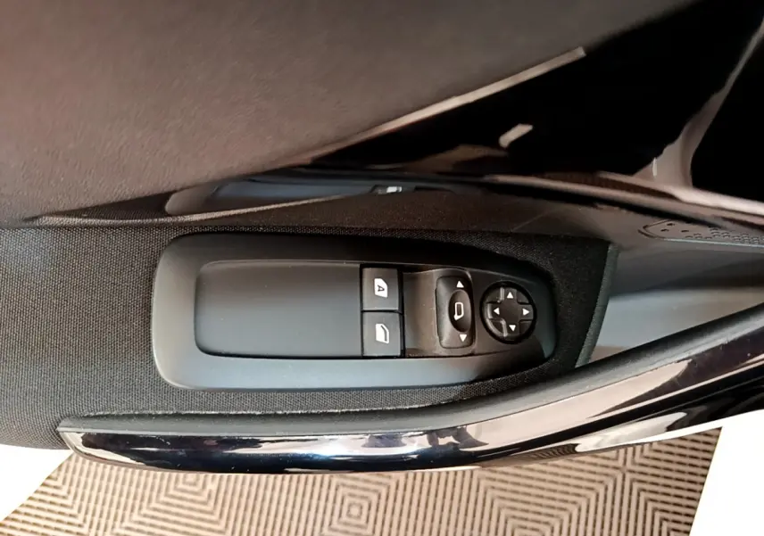 Gros plan sur les commandes électriques des vitres côté conducteur d'une Peugeot 208 blanche, finition Signature.