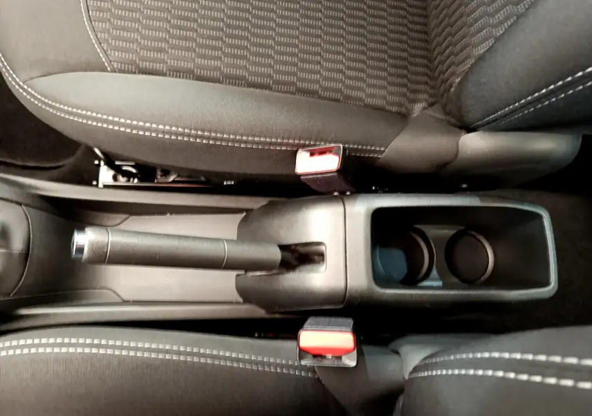 Gros plan sur le frein à main manuel et porte-gobelets entre les sièges noirs à surpiqûres blanches d'une Peugeot 208 blanche.