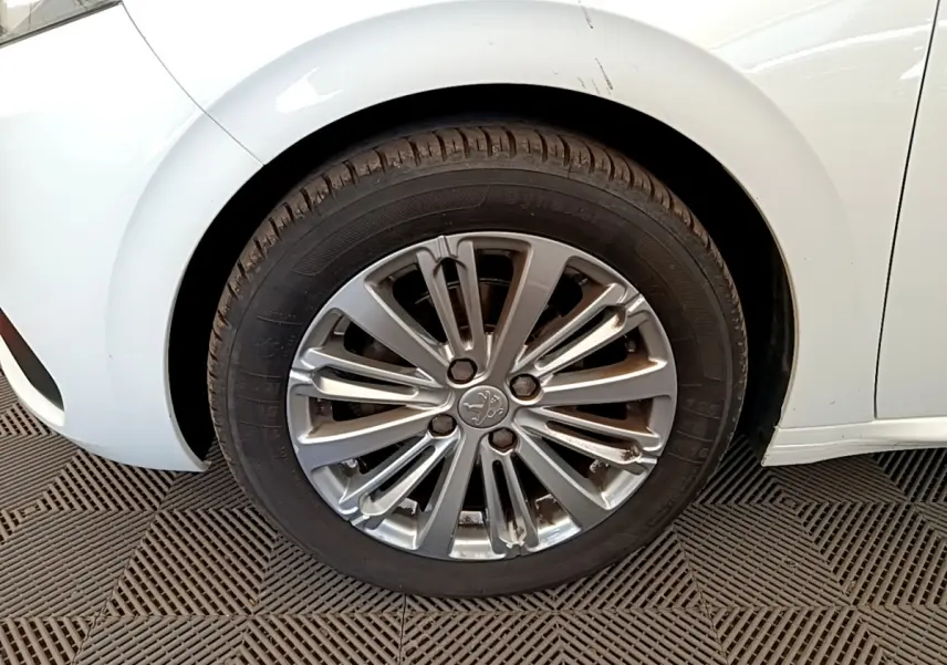 Gros plan sur la roue avant gauche d'une Peugeot 208 blanche, avec jante alliage au design moderne.