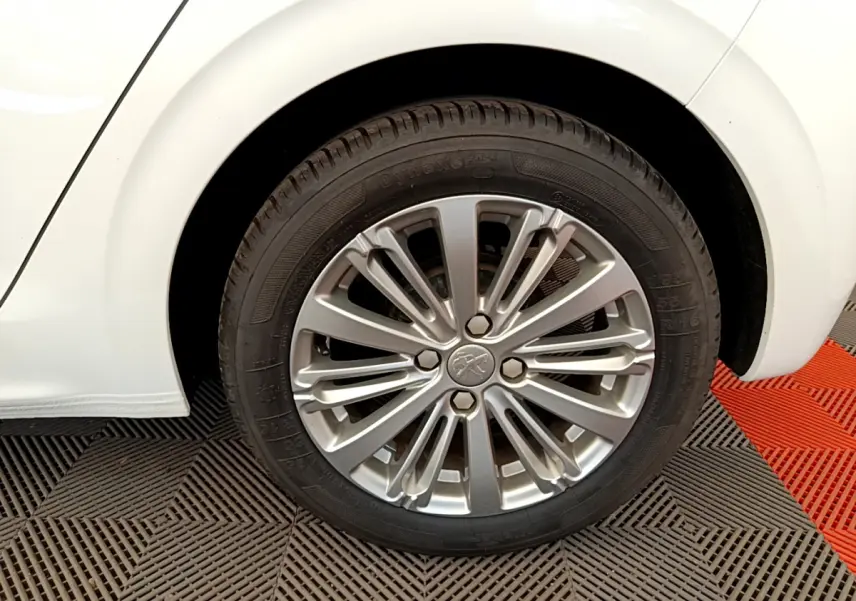 Gros plan sur la roue arrière droite d'une Peugeot 208 blanche avec jante alliage multi-branches.