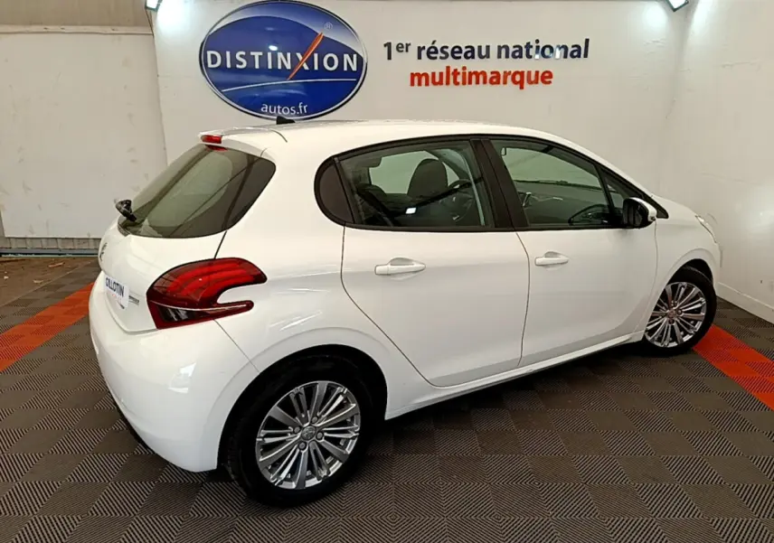 Vue 3/4 arrière droite d'une Peugeot 208 Puretech 82 Signature blanche en intérieur sur sol damier rouge et gris.